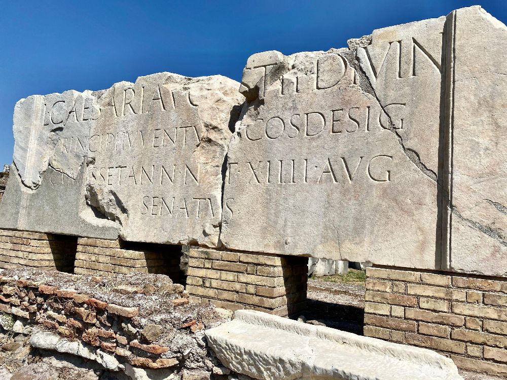 Iscrizione onoraria dedicata a Lucio Cesare (CIL VI 36908), figlio adottivo di Augusto, ricordato come princeps iuventutis e console designato. Rinvenuta nel 1899 presso la Basilica Aemilia, è oggi collocata nell'area del Foro Romano accanto alla basilica [Foto: Wknight94, Wikimedia Commons, CC BY-SA]