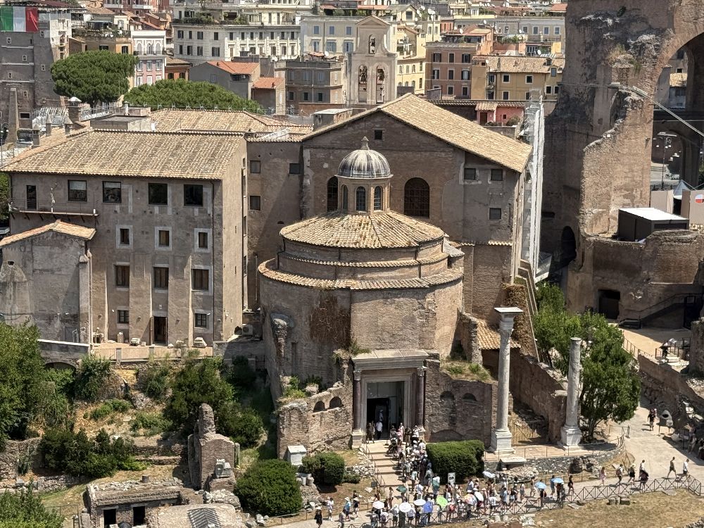 Il cosiddetto Tempio di Romolo visto dal Palatino. Al centro si riconosce il corpo circolare coperto a cupola, preceduto dal portale romano con la porta bronzea e le colonne di porfido. Tradizionalmente collegato a Valerio Romolo, figlio divinizzato di Massenzio, l’edificio fu successivamente incorporato nel complesso cristiano dei Santi Cosma e Damiano, visibile alle sue spalle. Sulla destra si innalzano le strutture della Basilica di Massenzio [Foto: Maria Teresa Natale, CC BY-NC-SA]